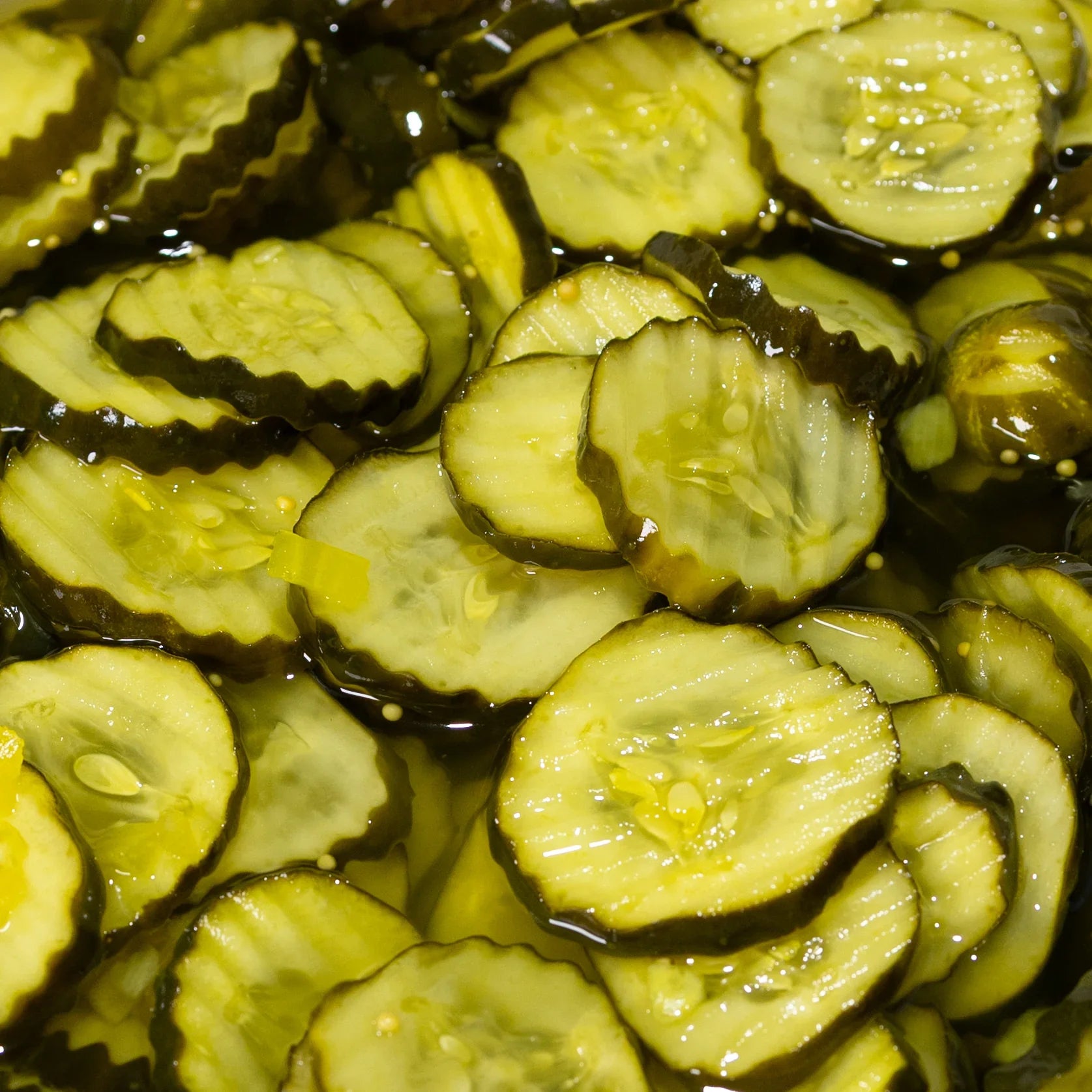 Close-up of sliced bread and butter pickles soaked in brine with wavy edges