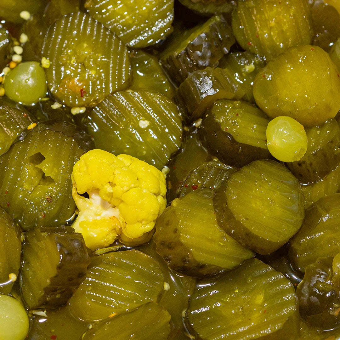 Close-up of candy heat pickle slices, with pickled cauliflower, and jalapenos in brine with chili flakes