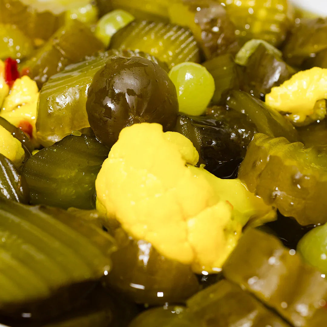 Close-up of candy sweet pickle slices with pickled vegetables including cauliflower and olives in brine