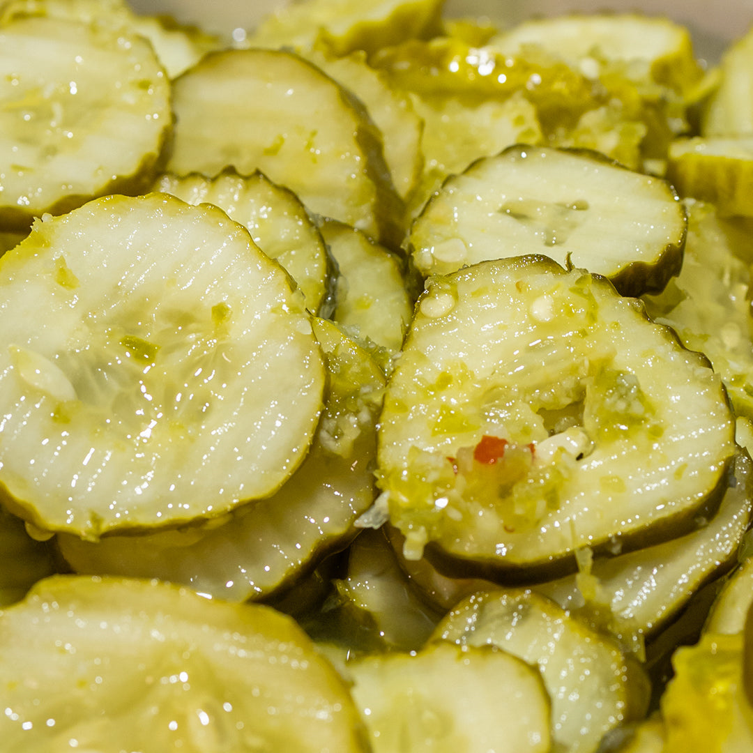 Close-up of extra spicy dill pickle slices with visible garlic and red chili flakes in brine