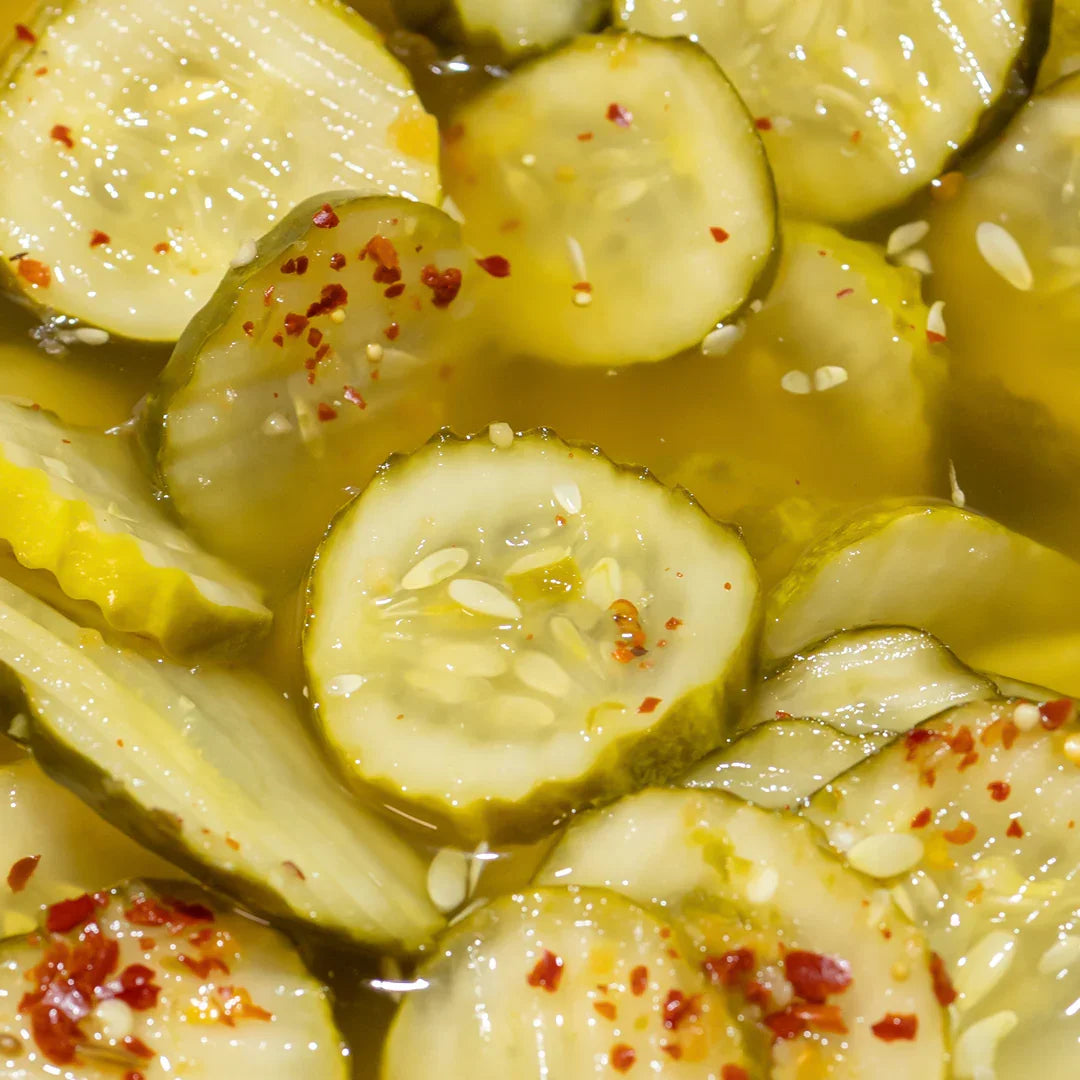 Close-up of spicy dill pickle slices with visible red chili flakes in brine