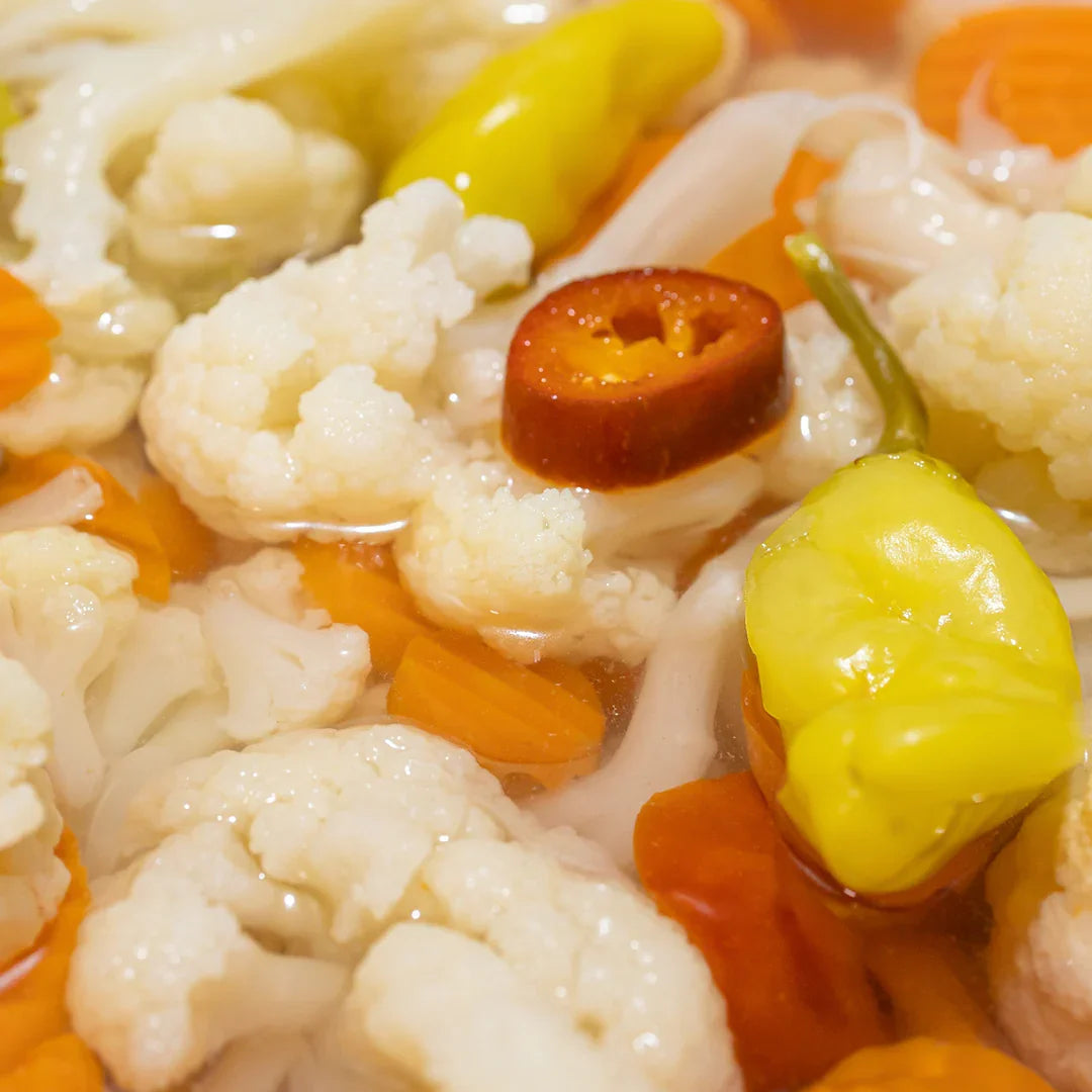 Close-up of pickled veggies inlcuding cauliflower, sliced carrots, yellow peppers, and red chili pieces in brine